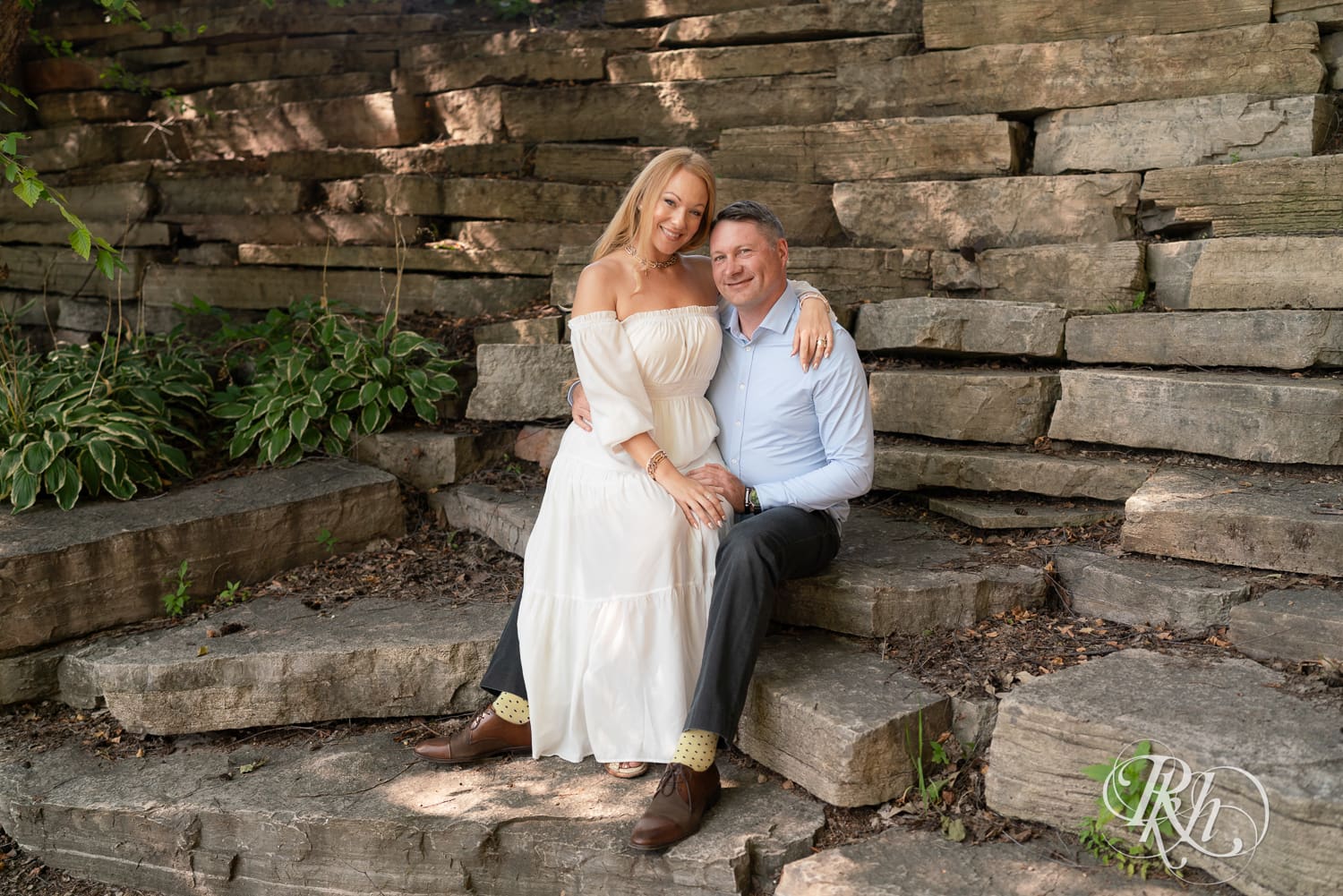 Man in jeans and blond woman in a white dress sit on rocks at Centennial Lake Park in Edina, Minnesota.