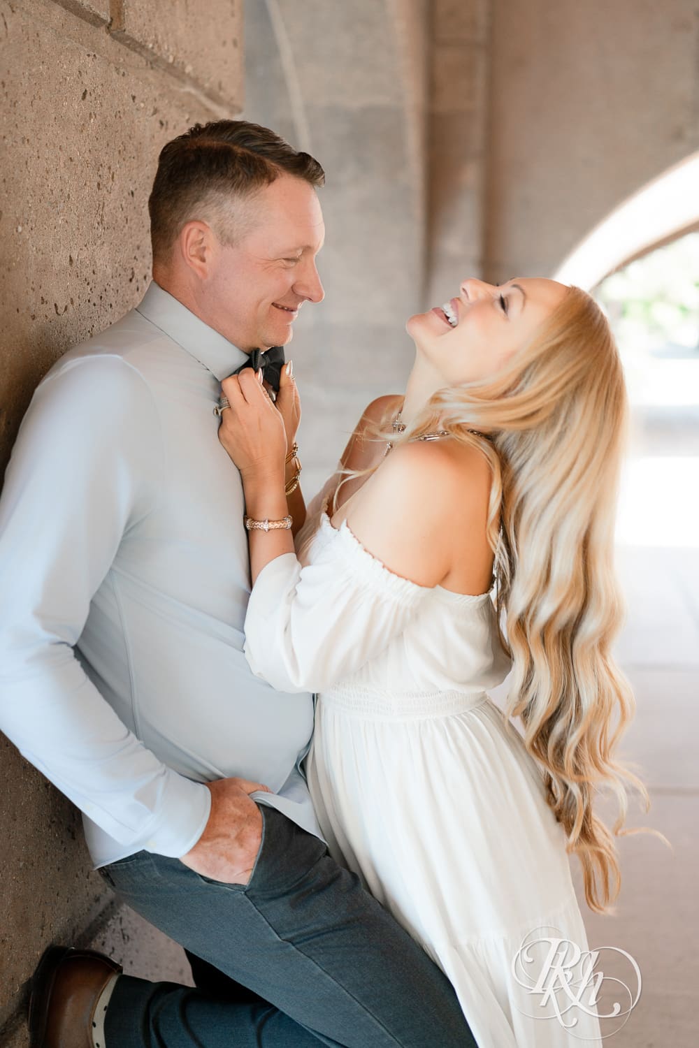 Man in jeans and blond woman in a white dress laugh under a bridge at Centennial Lake Park in Edina, Minnesota.