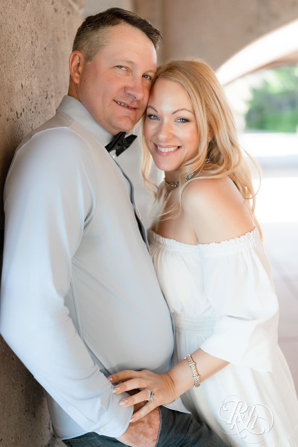 Man in jeans and blond woman in a white dress smile under a bridge at Centennial Lake Park in Edina, Minnesota.