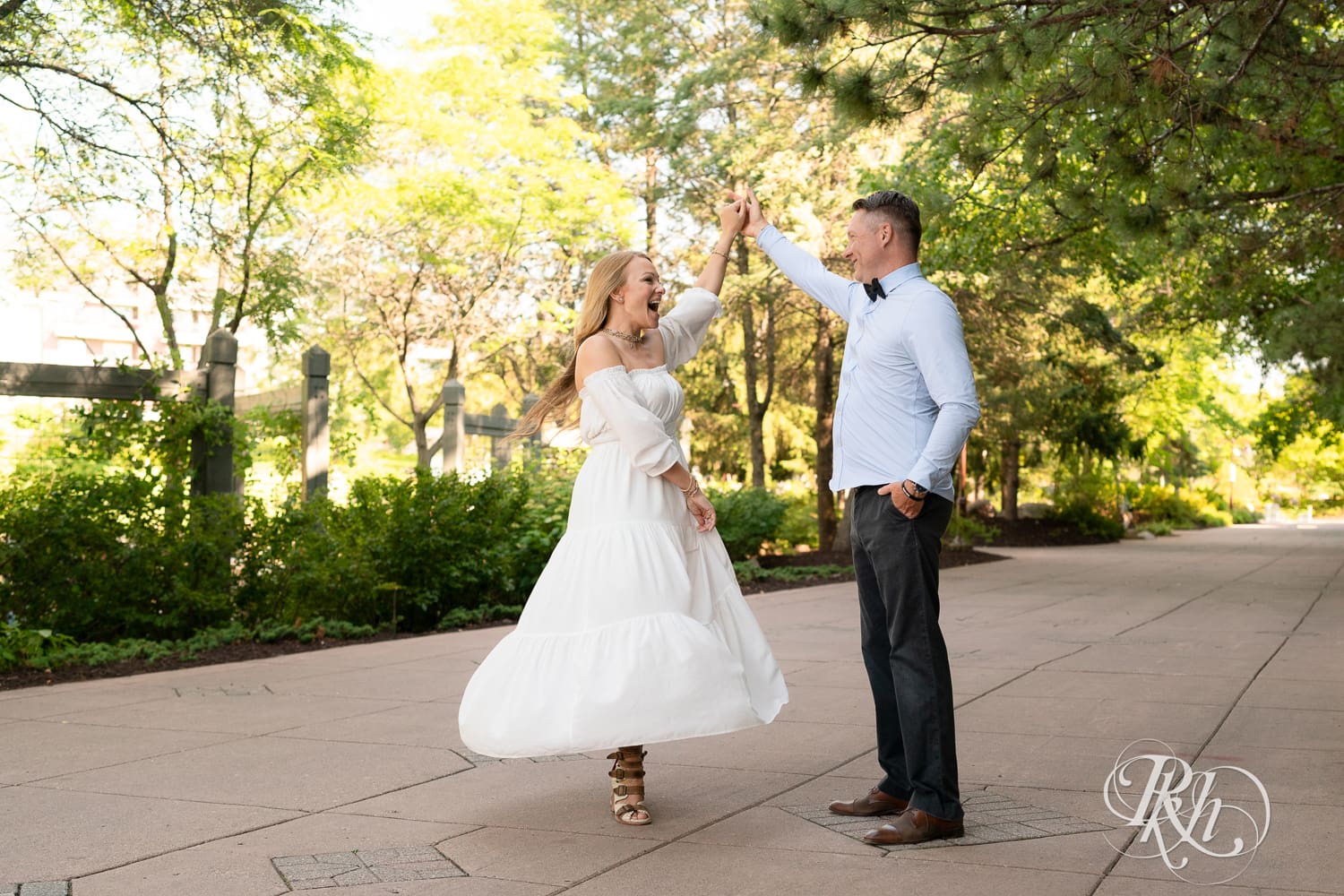 Man in jeans and blond woman in a white dress dance on path at Centennial Lake Park in Edina, Minnesota.