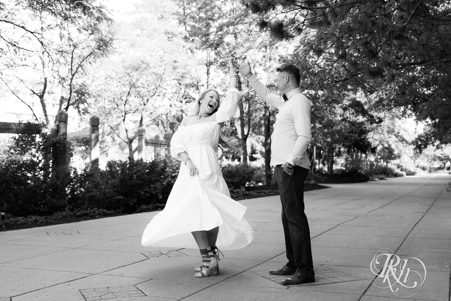 Man in jeans and blond woman in a white dress dance on path at Centennial Lake Park in Edina, Minnesota.